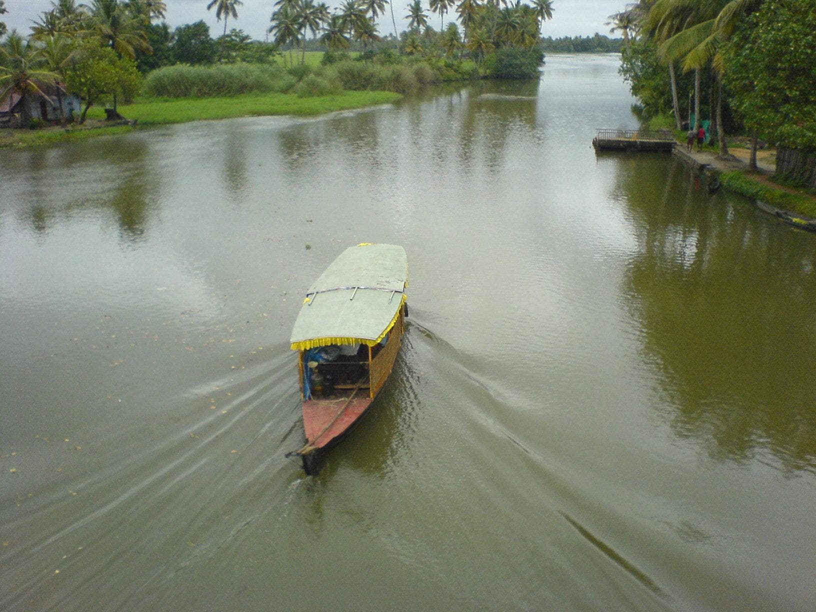 A small boat passing beneath a bridge on the Kumarakom backwaters